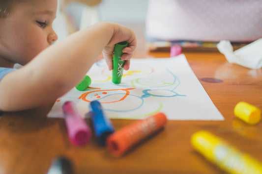 a little boy that is sitting at a table with some crayons
