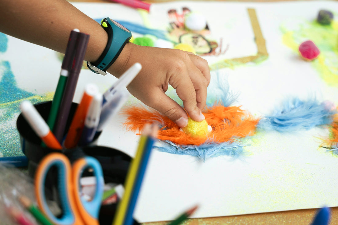Child's hand creating art with colorful feathers and markers