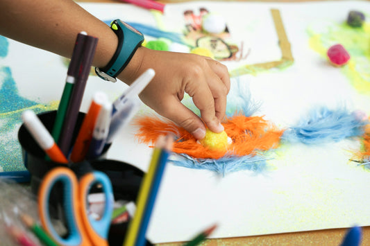 Child's hand creating art with colorful feathers and markers