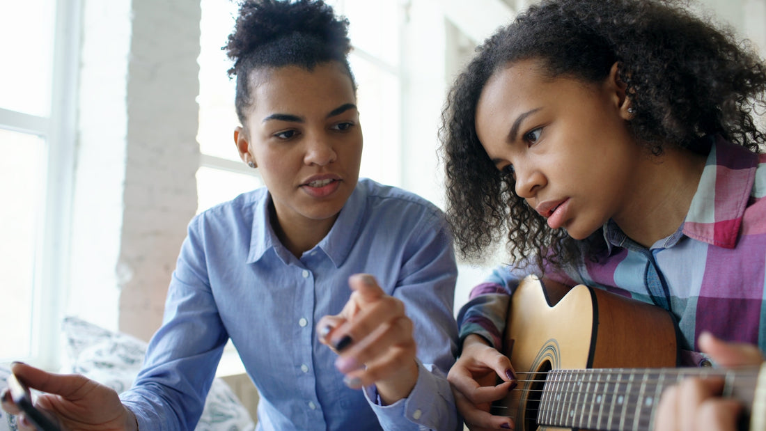 Two young women learning to play guitar together